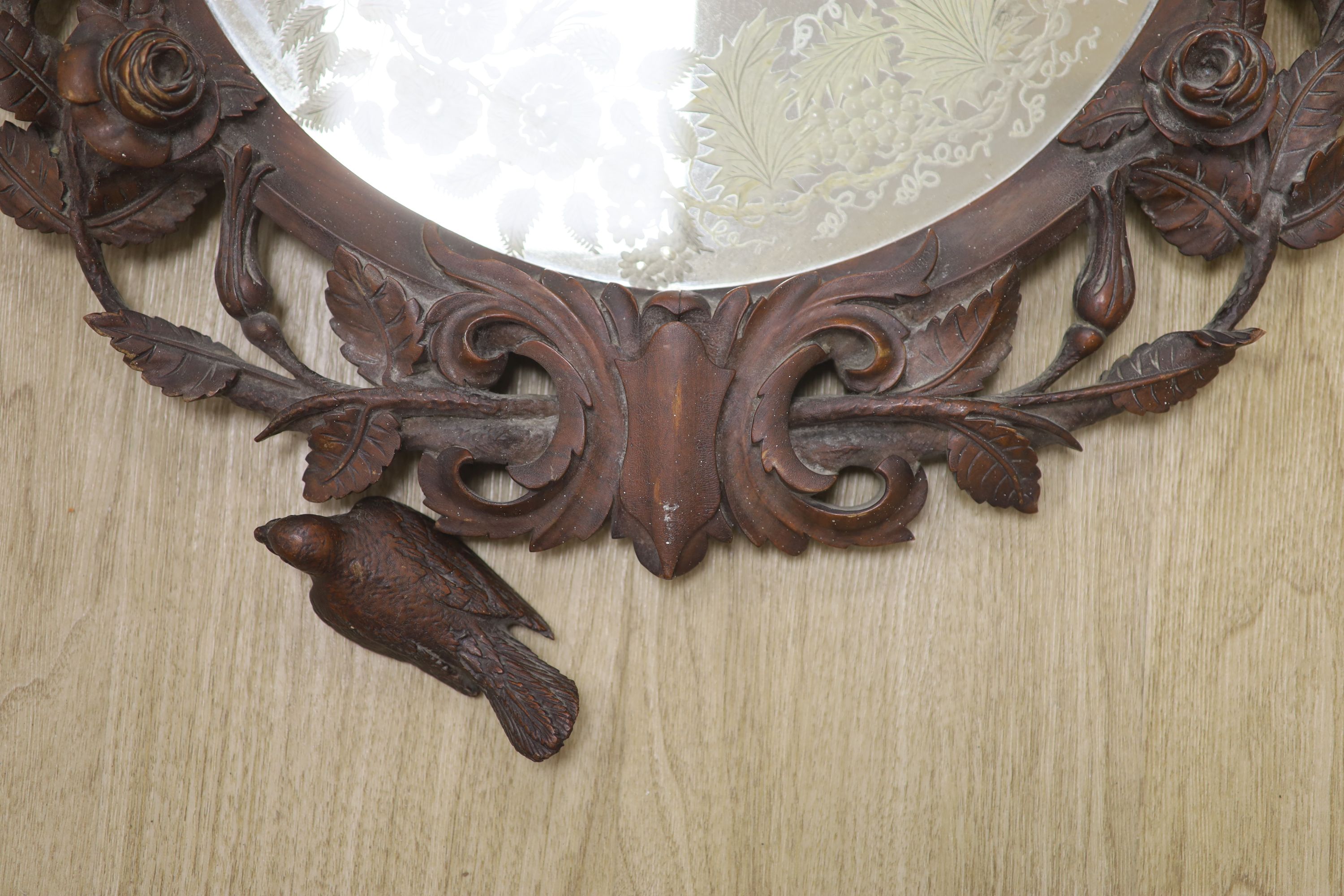 A 19th century Black Forest walnut wall mirror carved with roses and birds, diameter 56cm